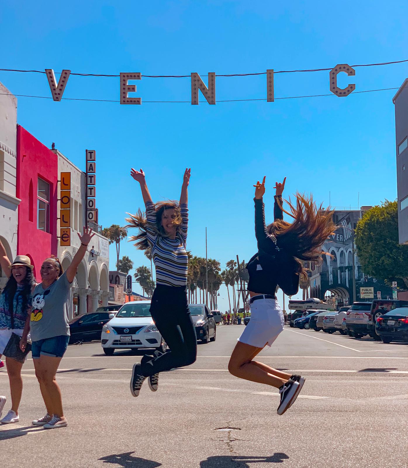 Alunas comemorando sob o letreiro de Venice Beach, em Los Angeles