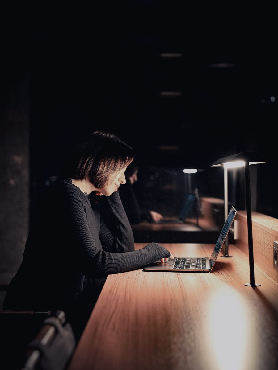 Profissional estudando inglês no laptop à noite, sob a luz de uma luminária de mesa