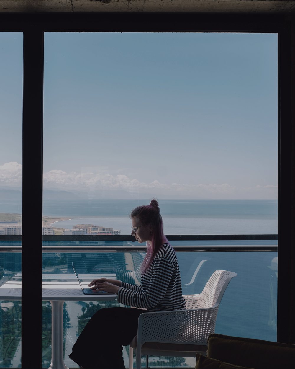 Profissional trabalhando de forma remota no laptop diante de uma janela com vista para o mar